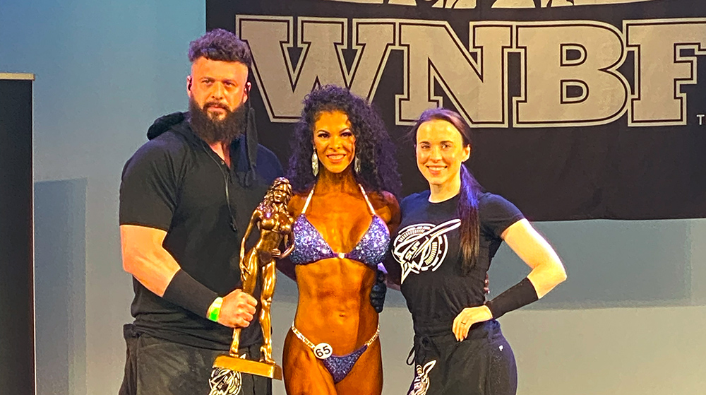 Natural Bodybuilding Coach Ryan Sullivan on stage with Bronwyn Kraus after winning her WNBF Bikini Pro Card at the 2021 INBF Naturalmania